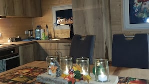 Un intérieur en bois avec une table à manger dressée pour quatre personnes, agrémentée d’un chemin de table à motifs floraux et de bougies.