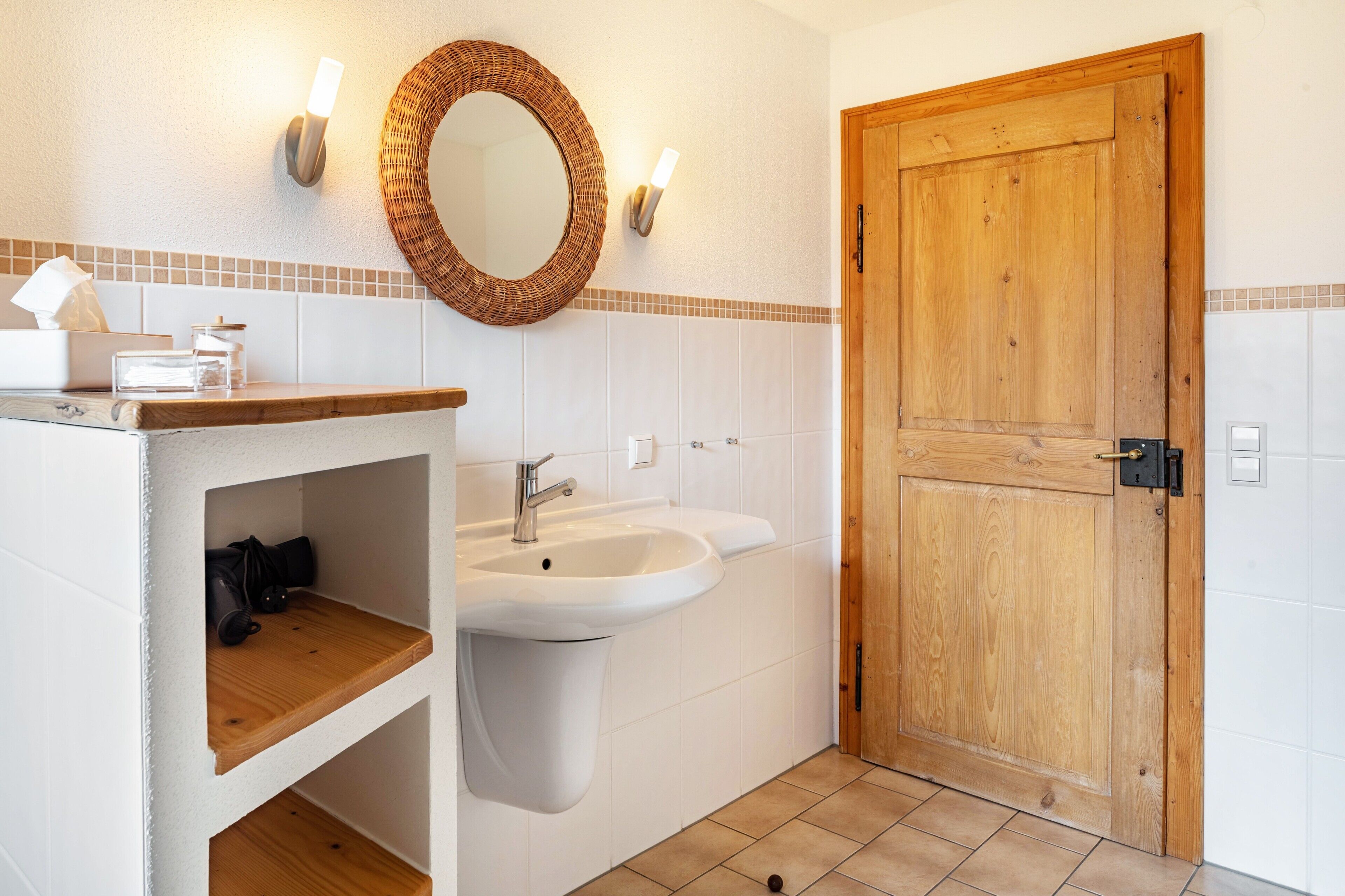 Une salle de bain avec une porte en bois, un lavabo, un miroir et une étagère contenant des articles de toilette.