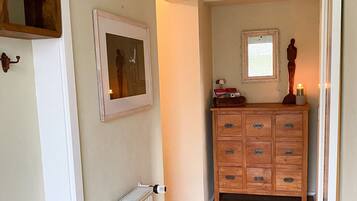 Een hal met een radiator, een houten dressoir met lades, een lijst met een foto aan de muur, en een klein raam.
