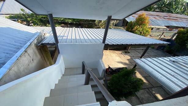 A staircase leading to a covered outdoor area with metal roofs and a view of neighboring buildings. - OYO Life 93154 White Kos Jenggala (Tanjung)