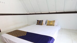 Un lit simple avec une couvre-lit blanche et bleue, deux oreillers à motifs jaunes et noirs, et un plafond blanc avec des poutres en bois.