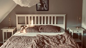 A bedroom with a white bed, a large ruffled window shade, a framed portrait on the wall, and bedside lamps. - "Holiday Apartment Frida" in the heart of Burkheim (Vogtsburg)