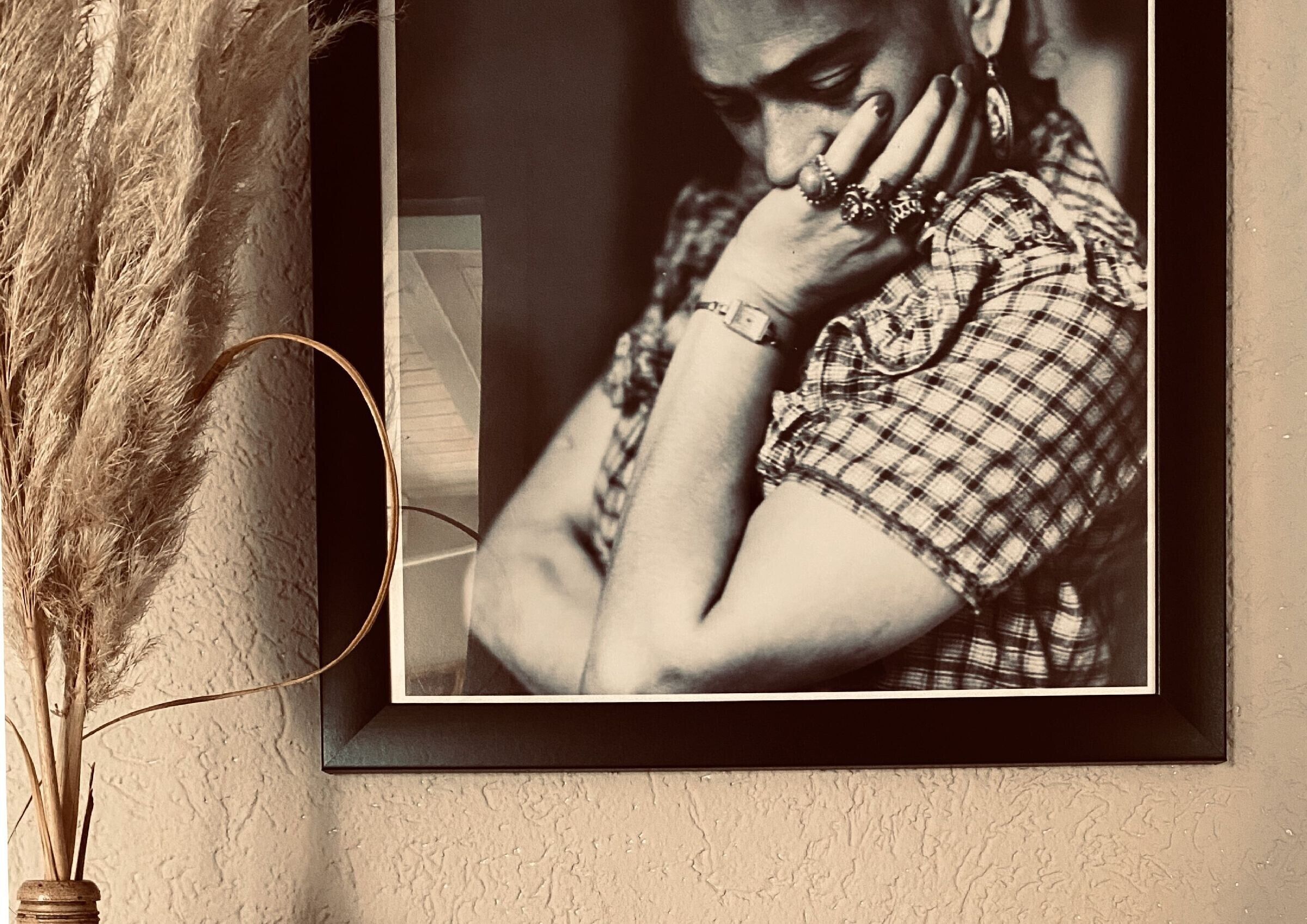Fotografia amb marc d'una persona amb camisa de ratlles, un ram de plantes seques i una paret amb relleu.