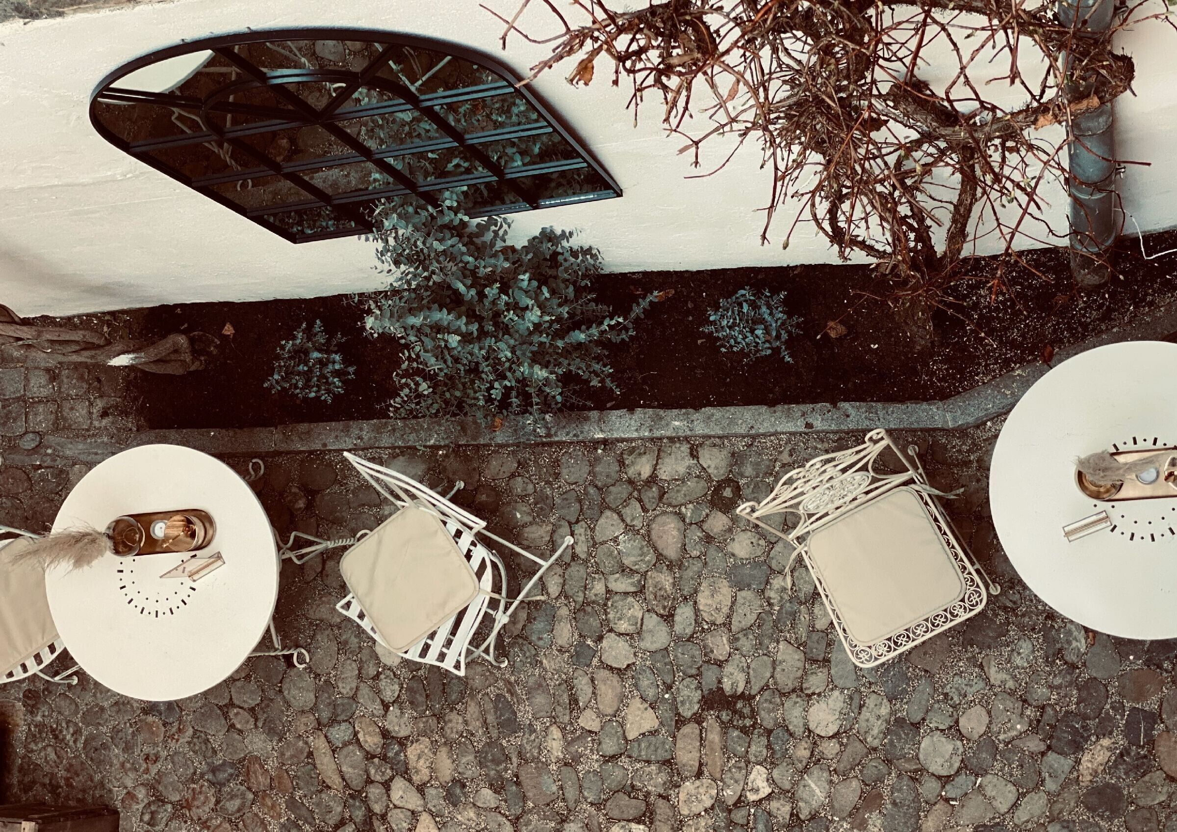Un patio con pavimento in pietra, tavoli e sedie bianche, una griglia in metallo e un albero.