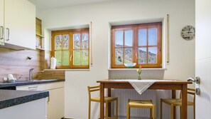 A kitchen with two windows, a sink, a table with chairs, and a wall clock.