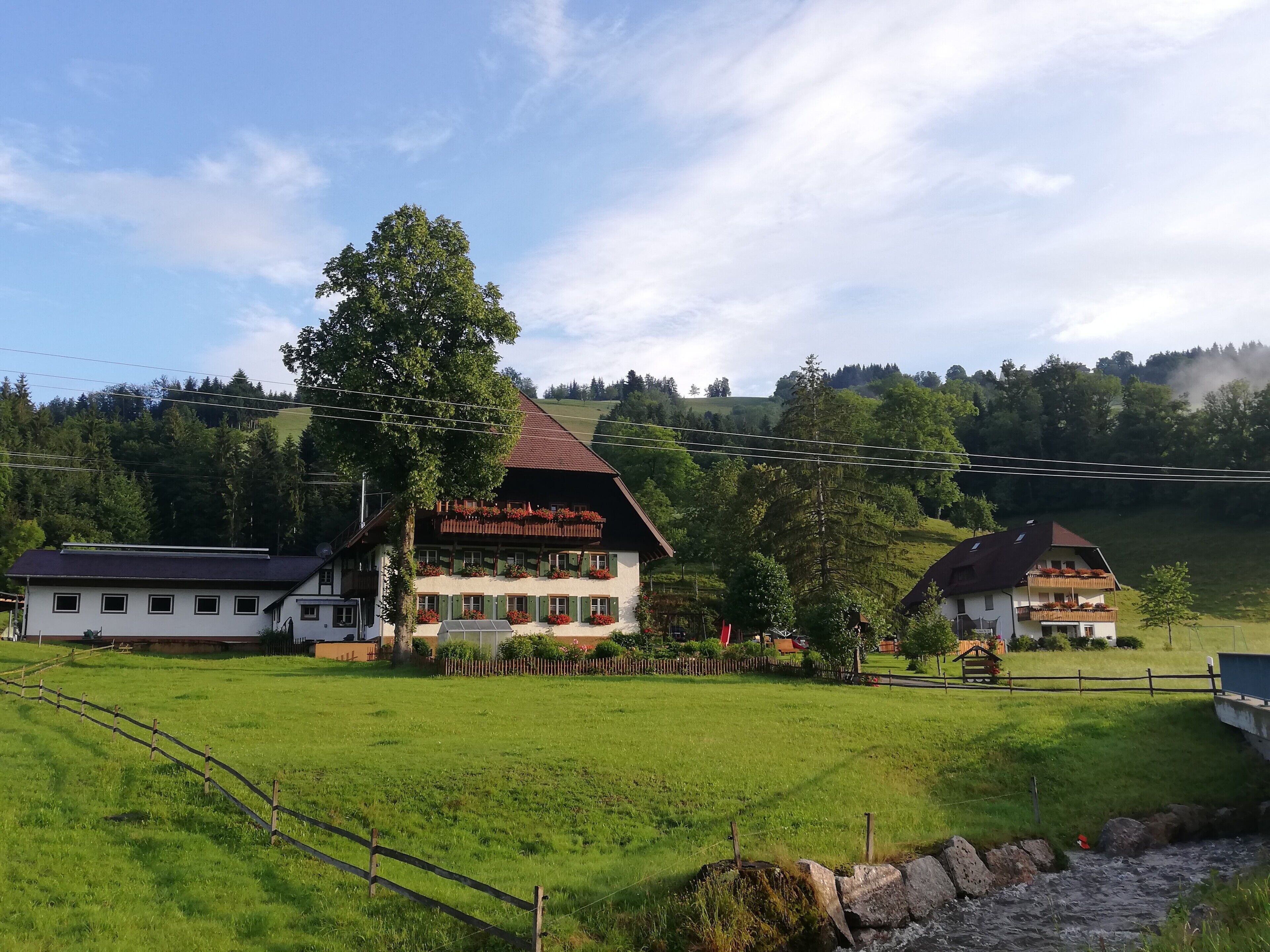 Ein Landhaus mit Balkon, umgeben von grünen Feldern und einer Hügelkulisse im Hintergrund.