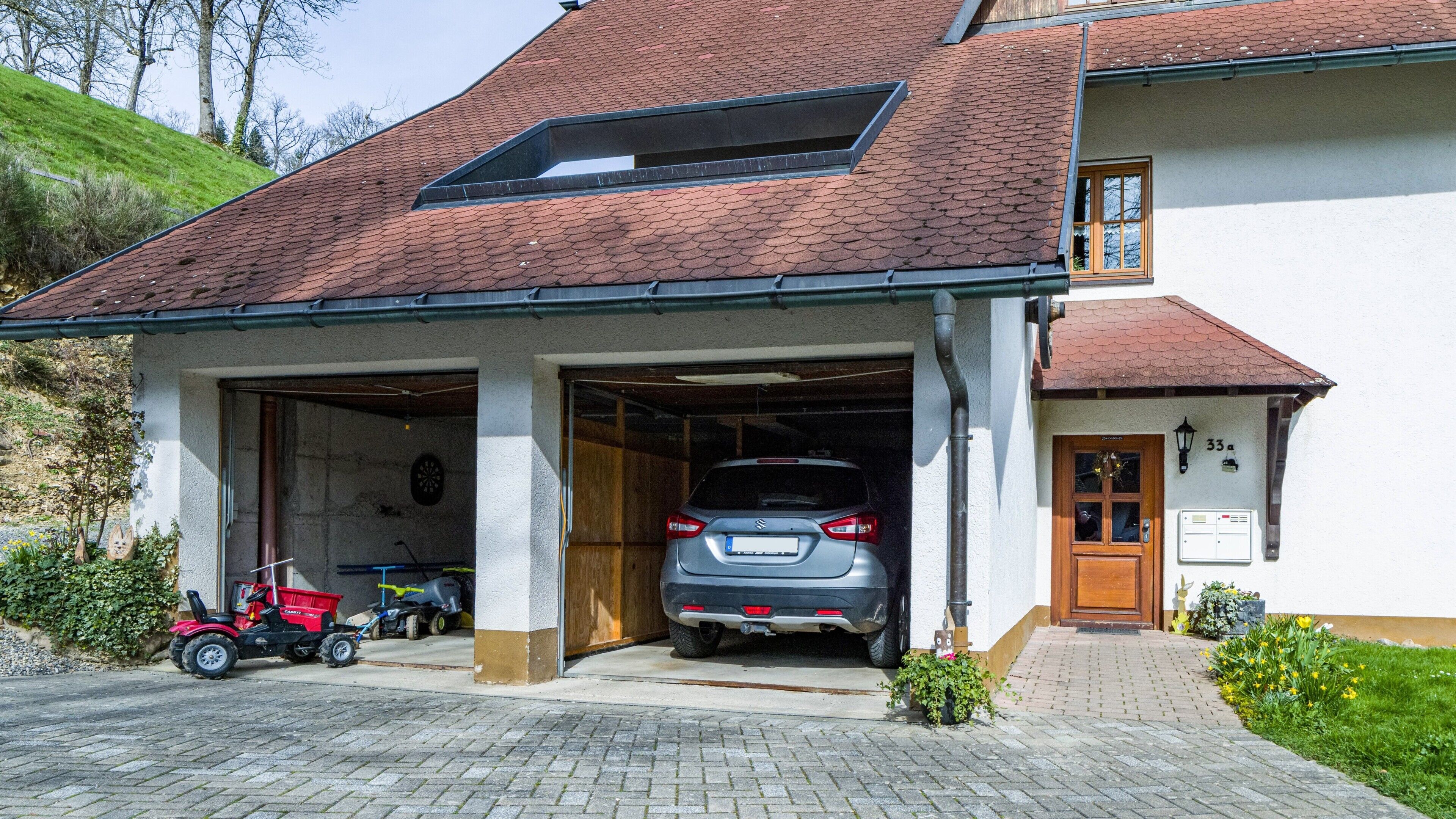 Ett tvåvåningshus med ett garage, ett rött tak och en liten trädgård.