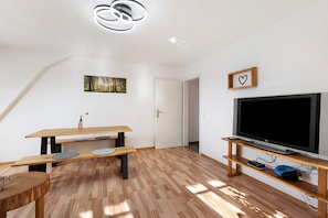 Un salon moderne avec un plancher en bois, une table à manger, un téléviseur posé sur un meuble en bois et un tableau encadré accroché au mur.