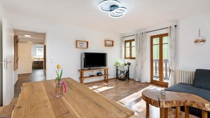 Een ruime woonkamer met een houten eettafel, een bank, een televisie en uitzicht op de omgeving.