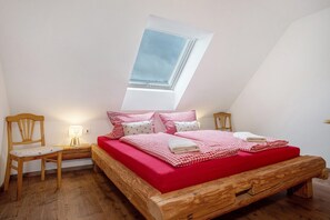 A bedroom with a wooden bed, red bedding, a skylight, and a nightstand with a lamp.