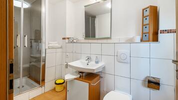 A bathroom with a shower, sink, toilet, and a mirror.