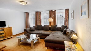 A modern living room with a sectional sofa, a glass coffee table, a wooden cabinet, and a TV. - Holiday Apartment "Kolibri" with Shared Terrace & Shared Garden (Naumburg (Saale))