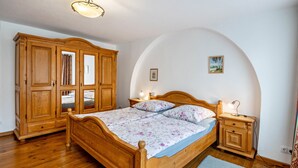 A wooden bed with a floral bedspread, a nightstand with a lamp, and a wardrobe in a room with wooden flooring and an arched ceiling. - Holiday Apartment "Kolibri" with Shared Terrace & Shared Garden (Naumburg (Saale))