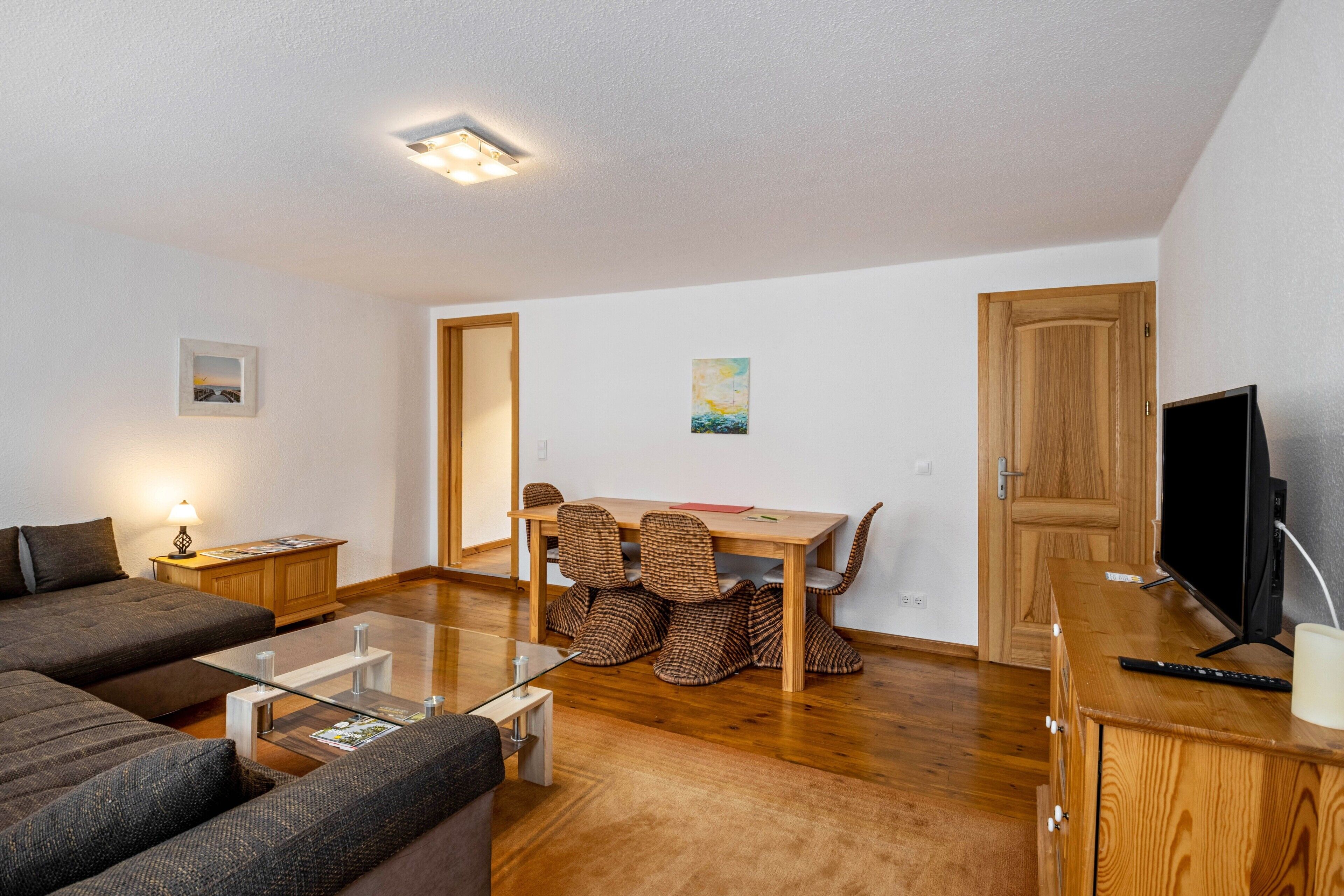 Un salon moderne comprenant un canapé, une table basse en verre, une table à manger en bois avec des chaises, un téléviseur et un meuble.