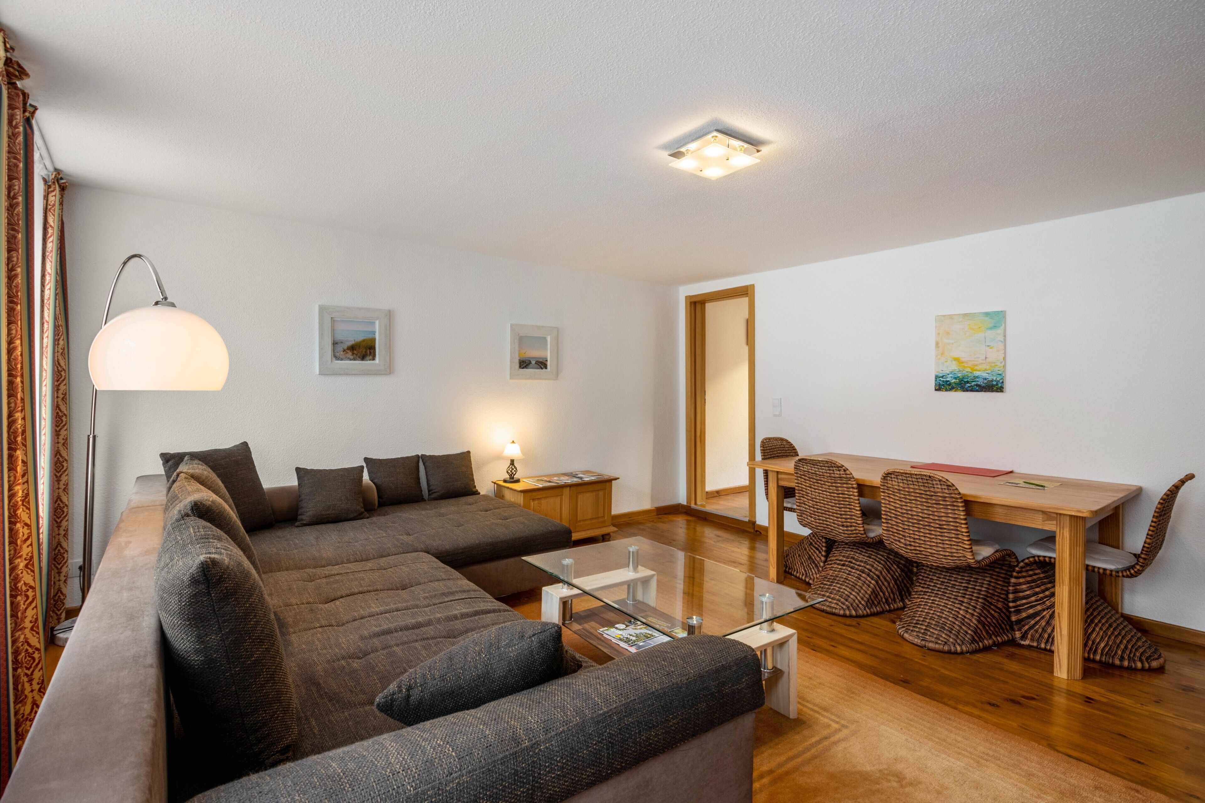 Een moderne woonkamer met een bank, een glazen salontafel, een lamp, een houten eettafel met stoelen en een plafondlamp.