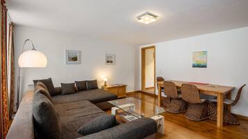 Een moderne woonkamer met een bank, een glazen salontafel, een lamp, een houten eettafel met stoelen en een plafondlamp.