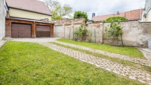 A residential area with a paved driveway, two garage doors, a brick wall, and a grassy lawn.