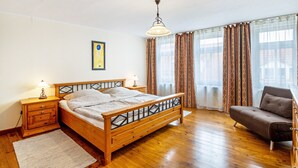 A bedroom with a wooden bed, a nightstand with a lamp, a sofa, and a window with curtains.