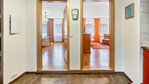 A hallway with wooden flooring, a clock, and a door leading to a room with a red carpet and a chair.