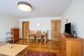 Una habitación con una mesa de comedor, sillas, un televisor sobre un mueble de madera y una lámpara en el techo.