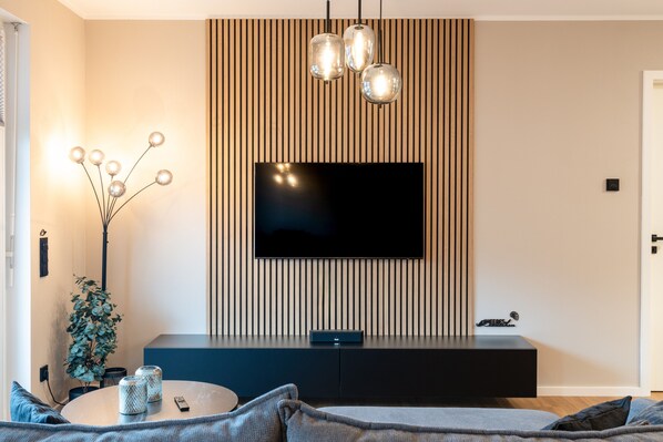 A modern living room with a flat-screen TV mounted on a wooden wall, a round coffee table, and a sofa.