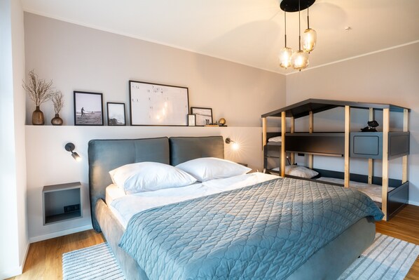 A modern bedroom with a bed, bedside tables, a wall-mounted shelf with pictures, and a built-in bench with storage.