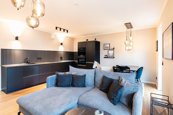 A modern living room with a sectional sofa, a kitchen area, and a dining space.