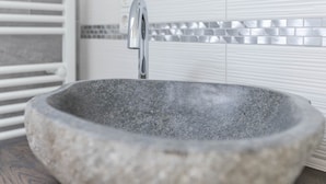 Ein Steinwaschbecken mit modernem Wasserhahn in einem Badezimmer mit weiß gefliesten Wänden und einem weißen Handtuchhalter.