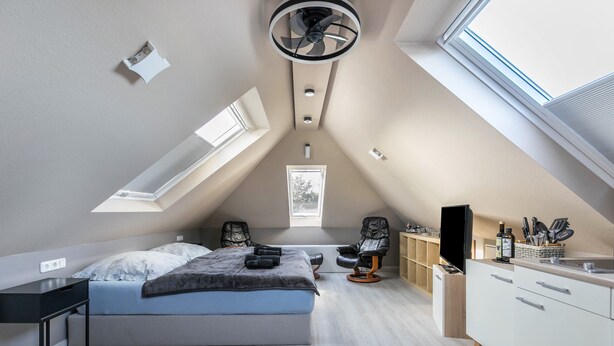 Ein Schlafzimmer mit einem Bett, einem Schreibtisch, einem Stuhl, einem Deckenventilator, einem Fenster und einem Einbauschrank.