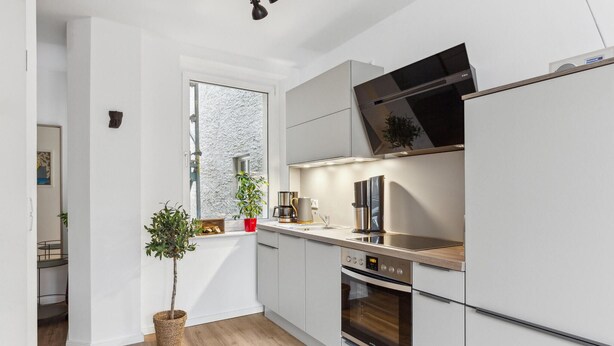 Een moderne keuken met witte kastjes, een ingebouwde oven, een magnetron en een koffiezetapparaat.