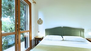 A bedroom with a large window, a bed with white bedding, a wooden nightstand, and a wall clock.