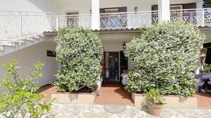 A courtyard with two large potted trees, a stone-tiled floor, and a white balcony railing.