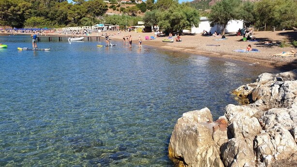 A coastal beach with clear water, rocky shoreline, and beach umbrellas.
