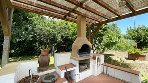 An outdoor patio with a brick floor, a wooden pergola, a brick oven, and potted plants.