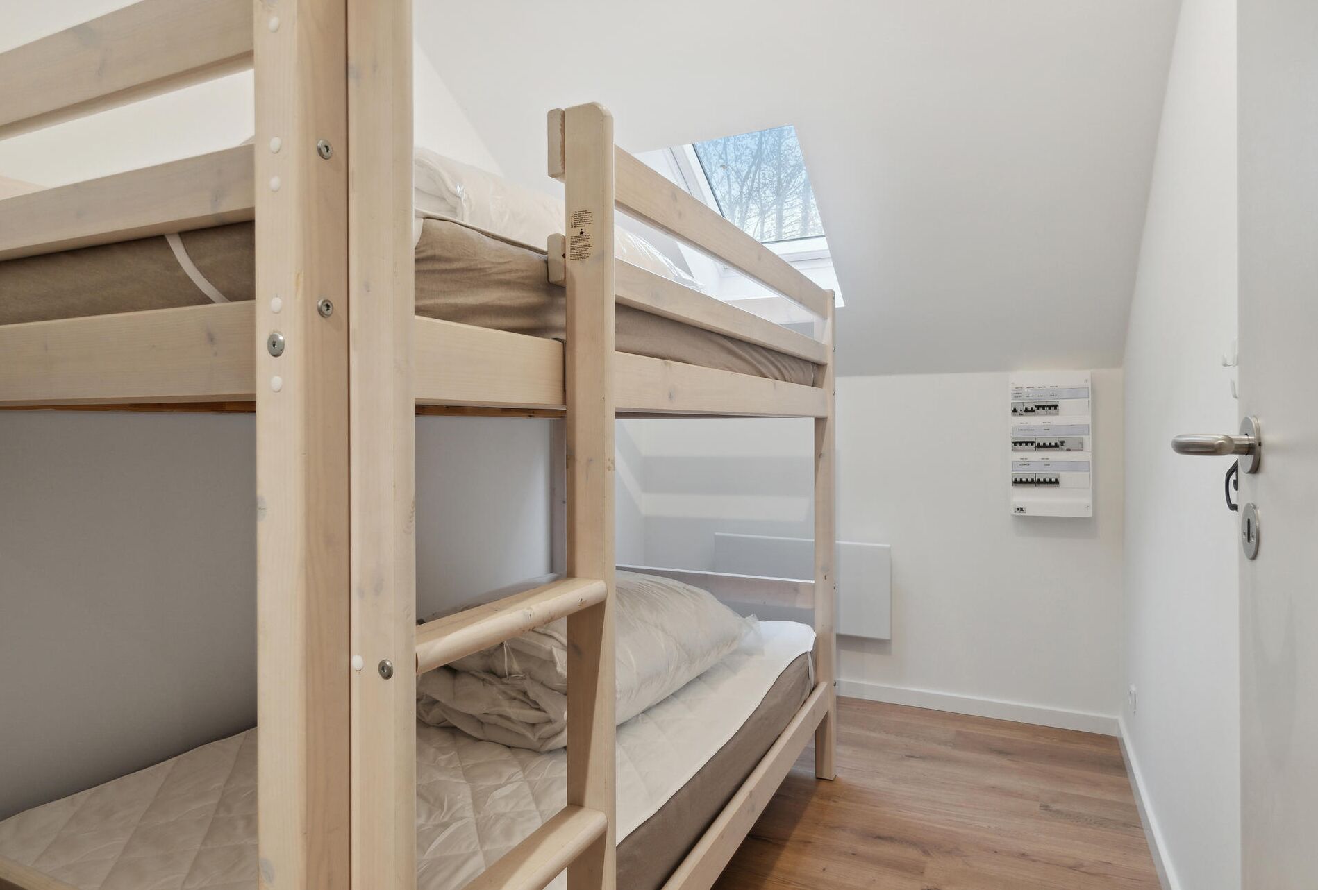 Een studentenkamer met stapelbedden, een dakraam en een thermostaat aan de muur.