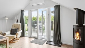 Une pièce chaleureuse avec un canapé, une table, une cheminée et une porte-fenêtre coulissante donnant sur un espace extérieur.