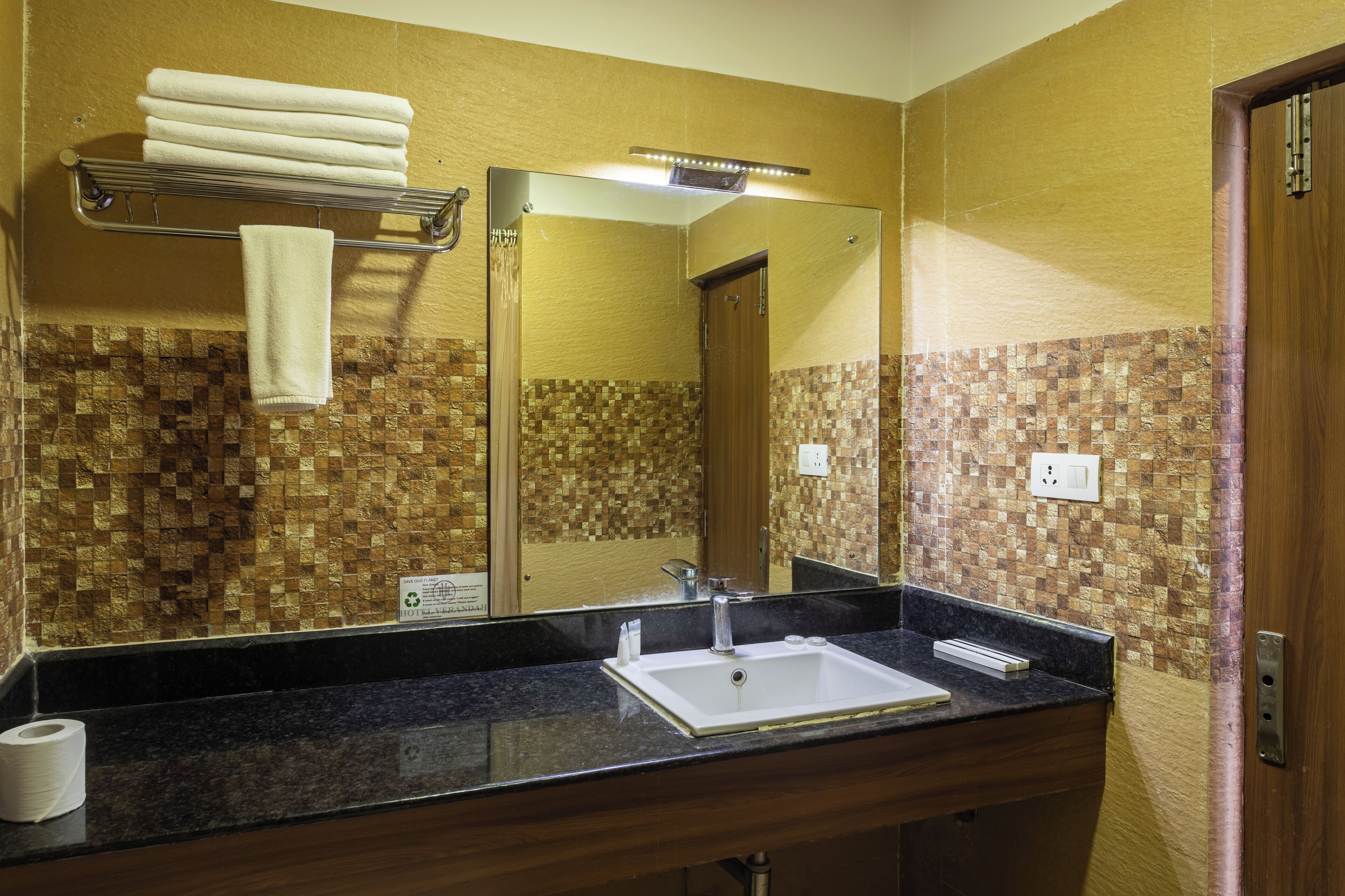 Une salle de bain équipée d’un lavabo, d’un miroir, d’un porte-serviettes et d’un mur recouvert de mosaïques.