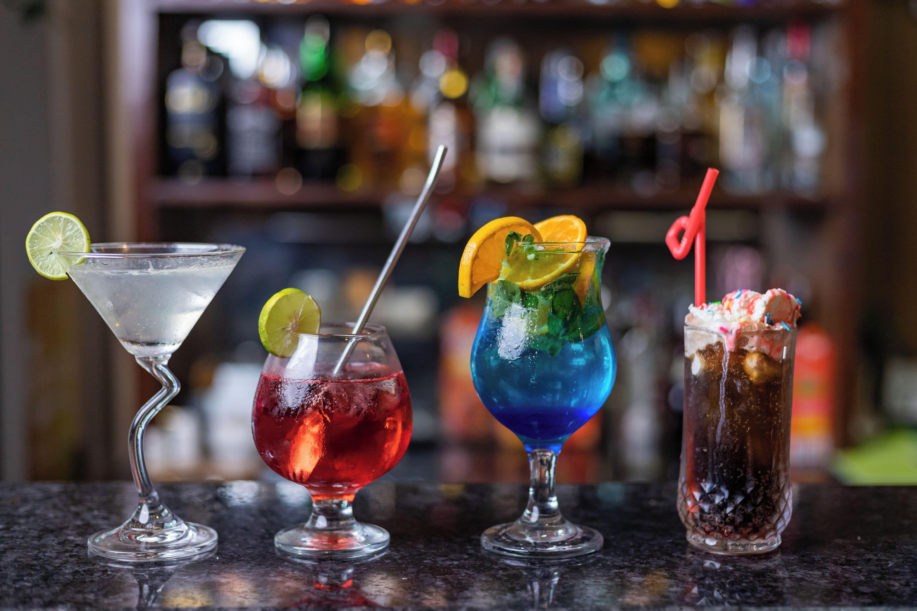 Four cocktails on a bar counter with a blurred background of bottles.