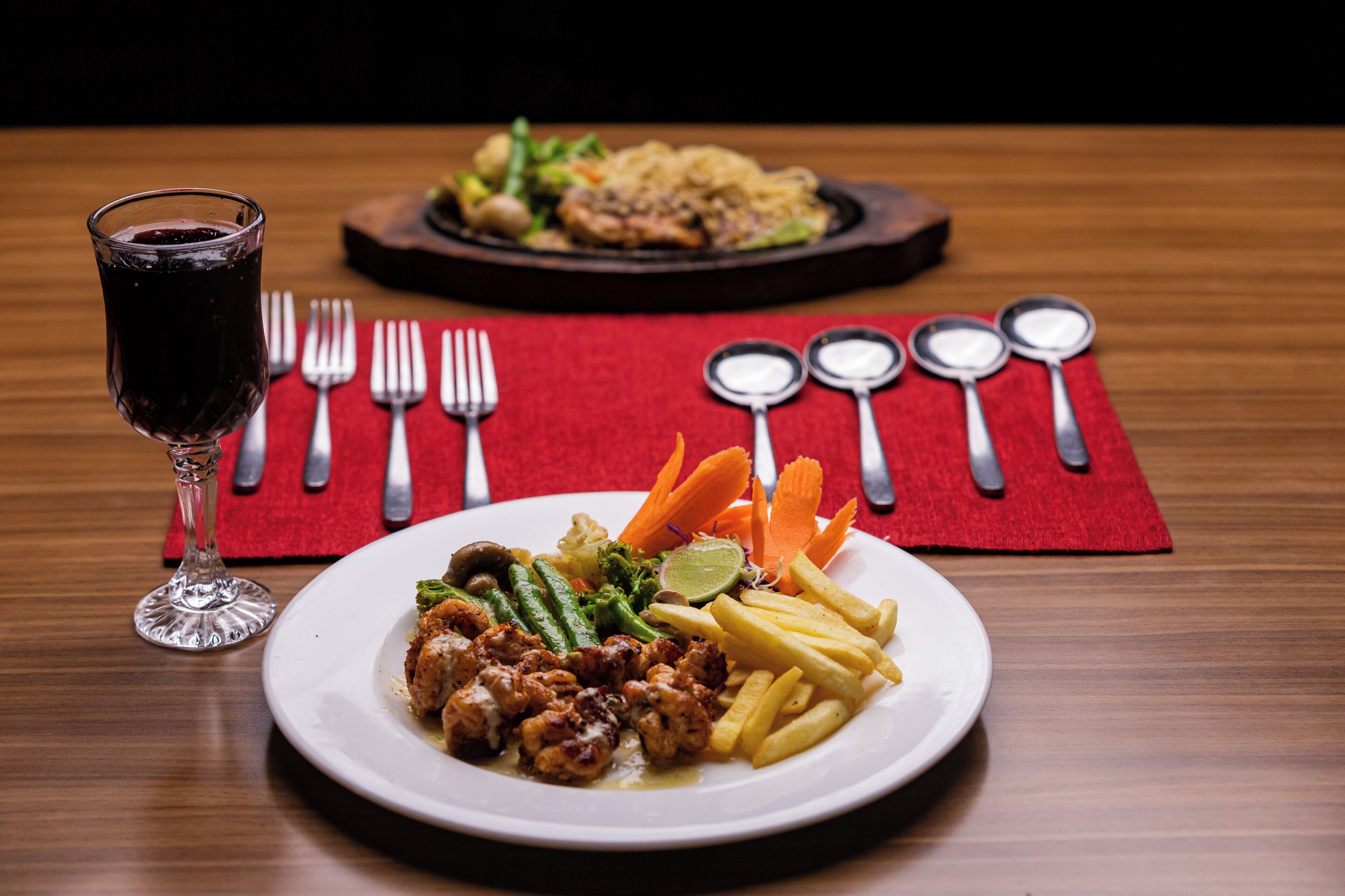 A dining table with a plate of food, a glass of red drink, and cutlery.