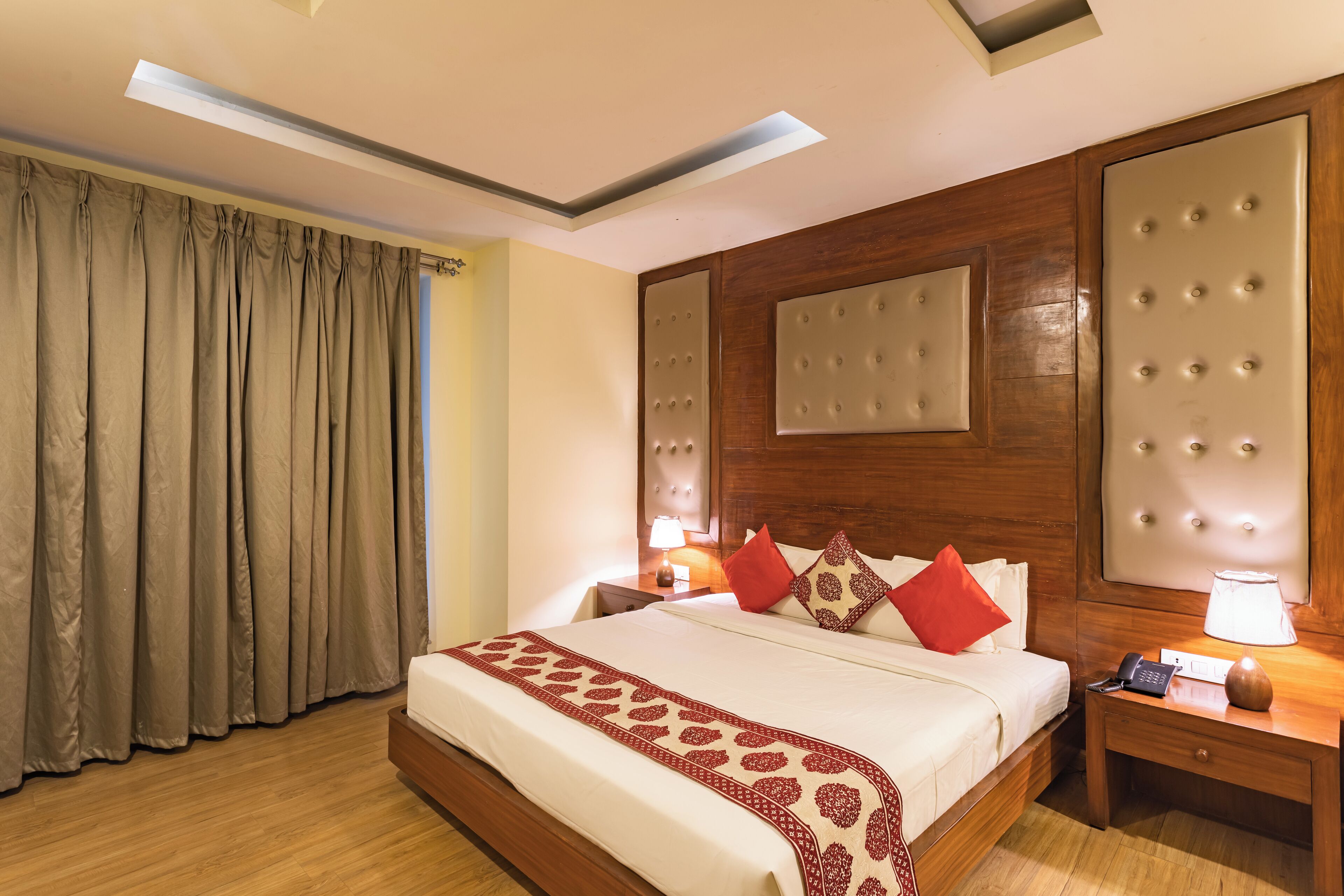 A hotel room with a large bed, wooden headboard, bedside tables, and a ceiling light fixture.