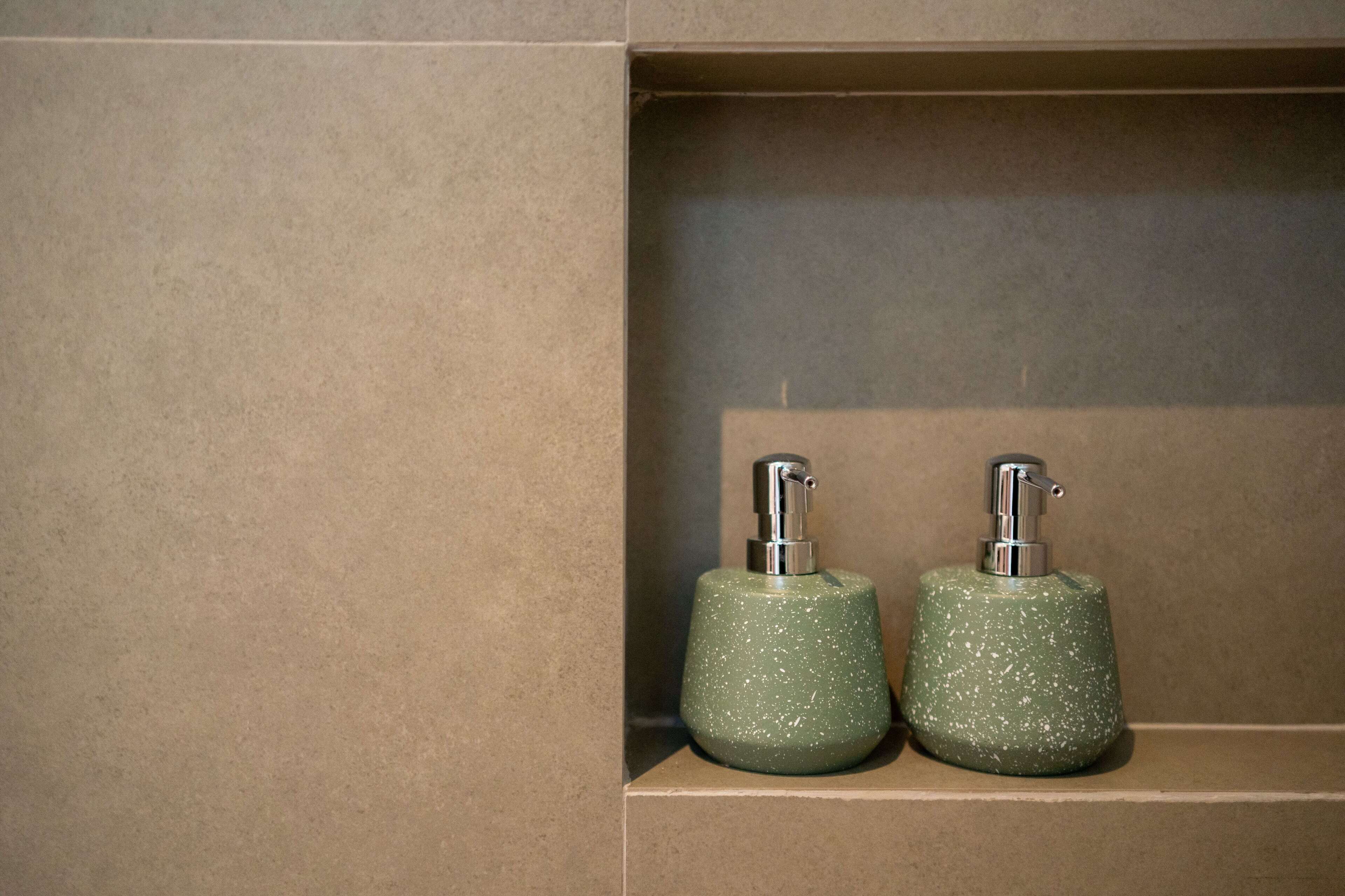 Two green soap dispensers in a bathroom shelf.