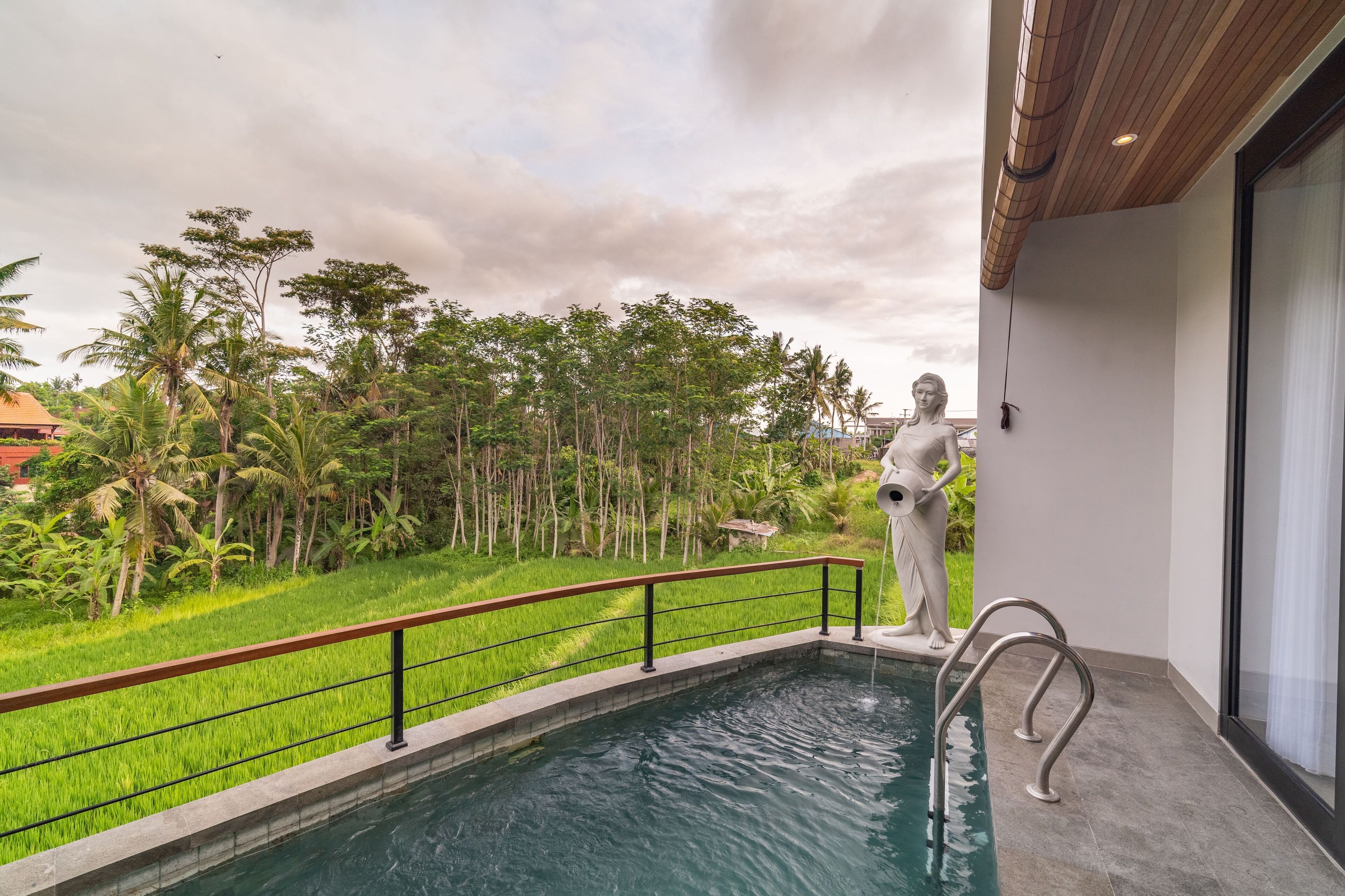 A swimming pool with a statue, surrounded by lush greenery and a view of a residential area.