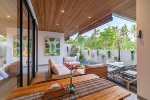 A modern indoor space with a wooden ceiling, a pool, and a view of lush greenery outside. - D'Macho Villas Ubud (Mas)