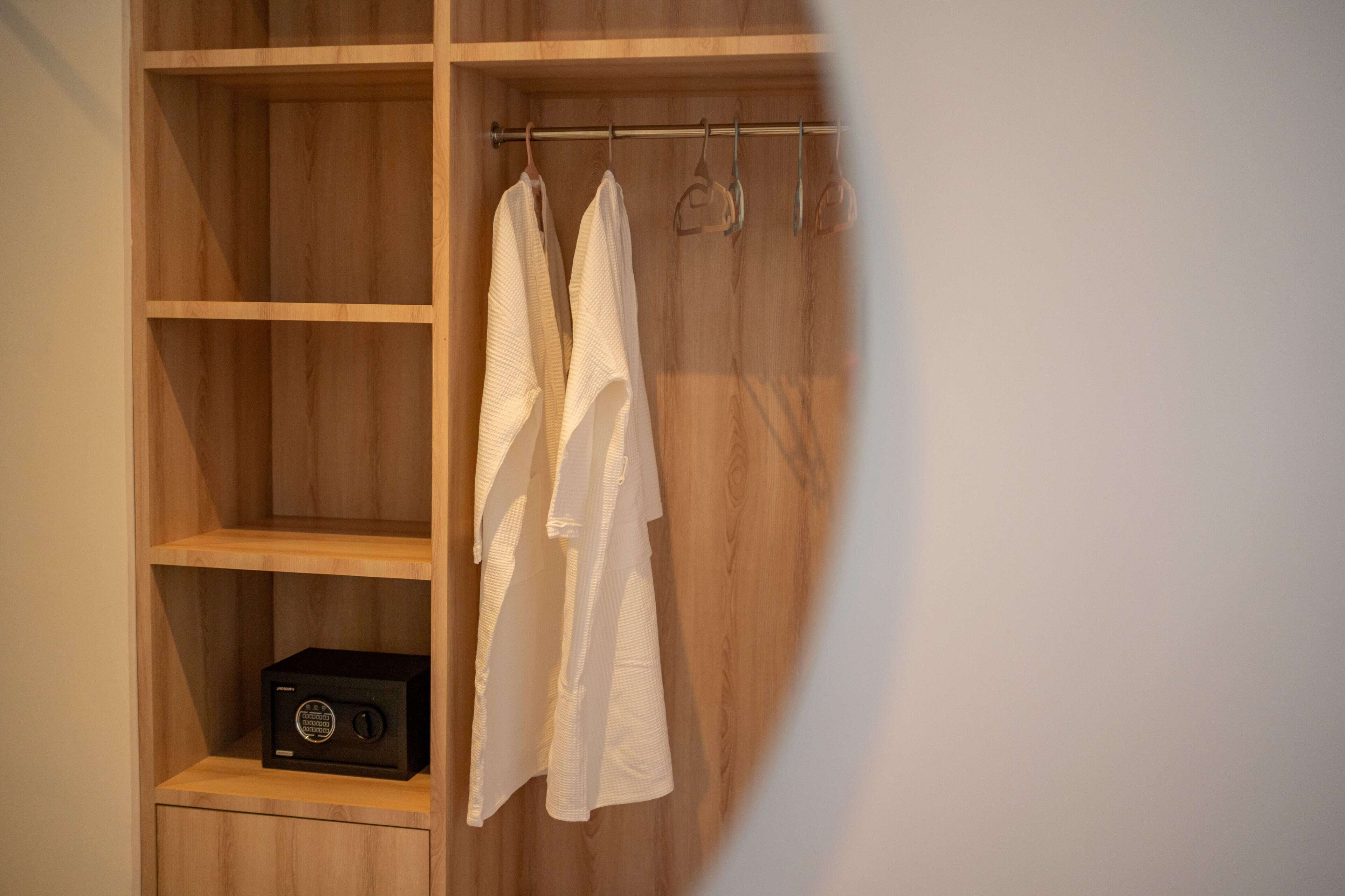 A wooden wardrobe with shelves and hanging space, containing a black radio and white towels.