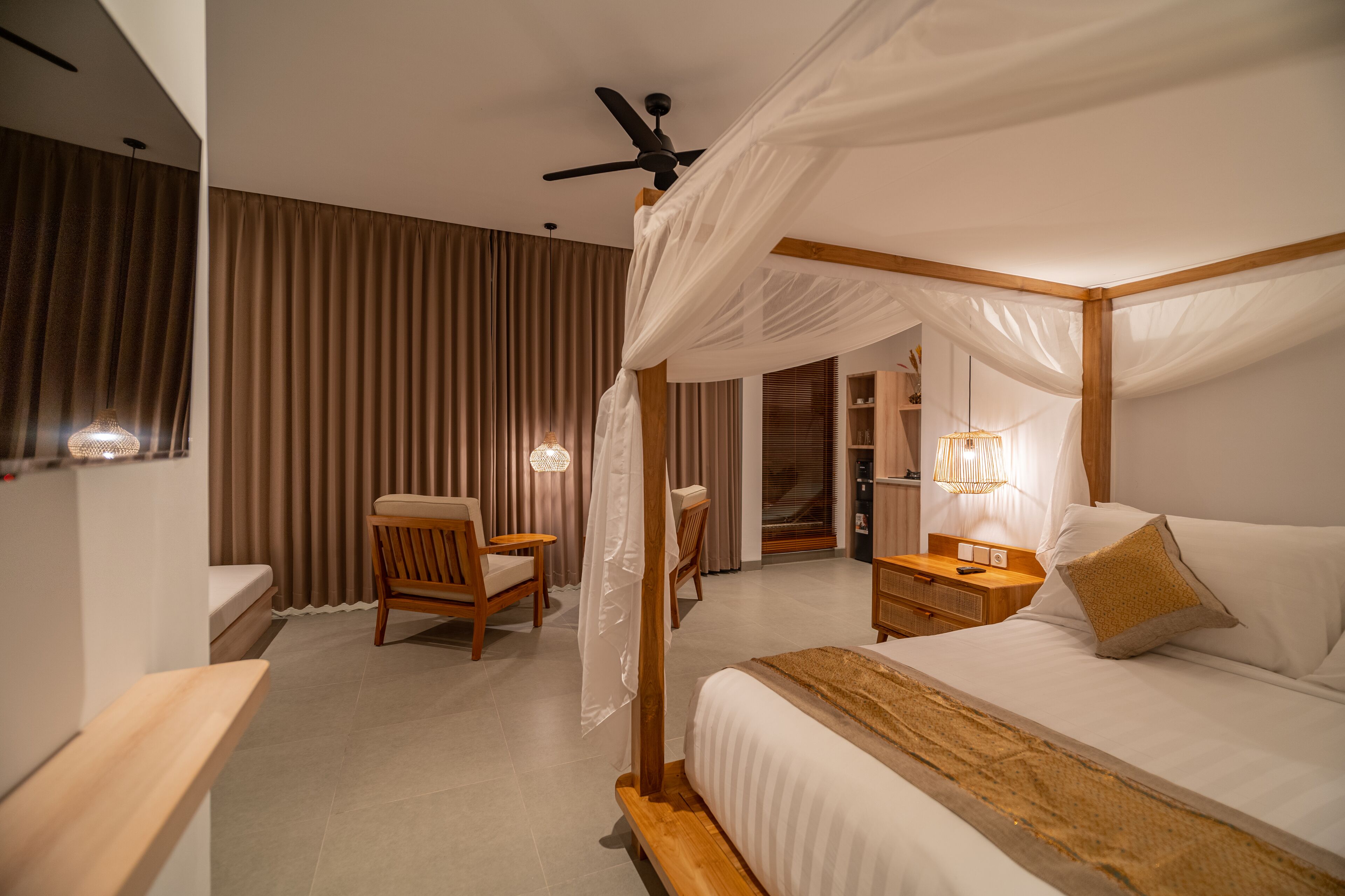 A four-poster bed with a canopy, a bedside table with a lamp, a chair, and a bedside table with a remote control.