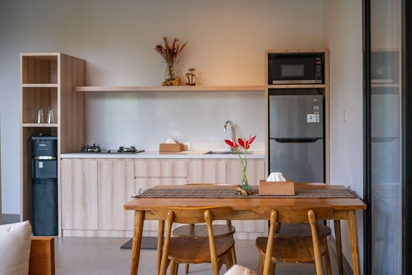 A modern kitchen with wooden cabinets, a microwave, and a refrigerator. There is a dining table with chairs and a vase with flowers on the counter. - D'Macho Villas Ubud (Mas)