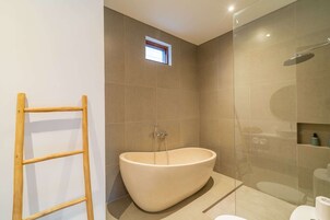 Un baño moderno con una bañera independiente, un box de ducha con mampara de vidrio y un ventanal pequeño.