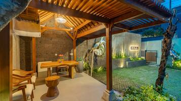 Uma área de pátio ao ar livre com pérgola de madeira, mesa de jantar com cadeiras e parede de pedra.