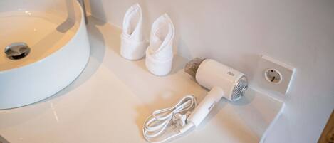 A white bathroom sink, a hairdryer, and a pair of white towels on a white countertop.