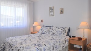 Et soveværelse med en seng, to sengeborde, en lampe og et vindue med lette gardiner.